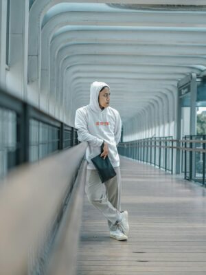 Young adult in stylish streetwear posing on a modern bridge, embodying urban fashion vibes.
