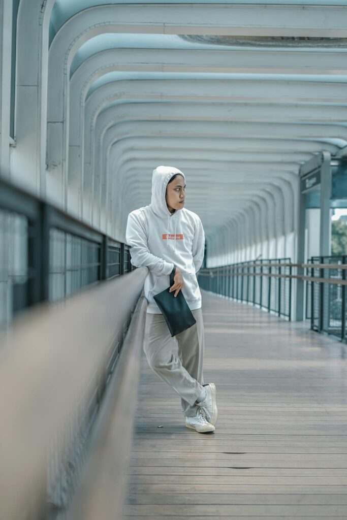 Young adult in stylish streetwear posing on a modern bridge, embodying urban fashion vibes.
