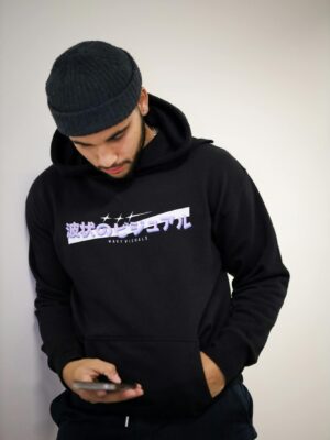 Young man wearing a hoodie and hat, looking down at smartphone indoors.